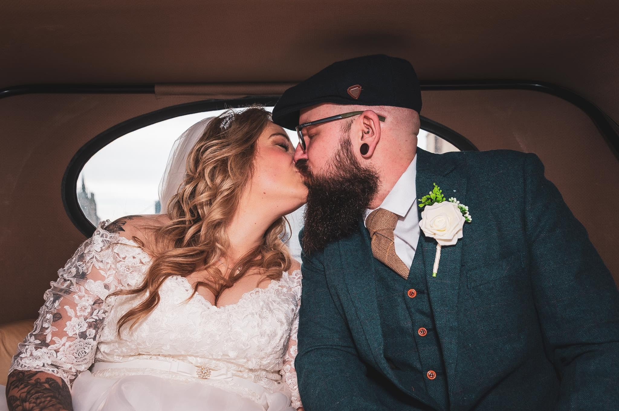 Newly married couple sharing a kiss inside a vintage wedding car